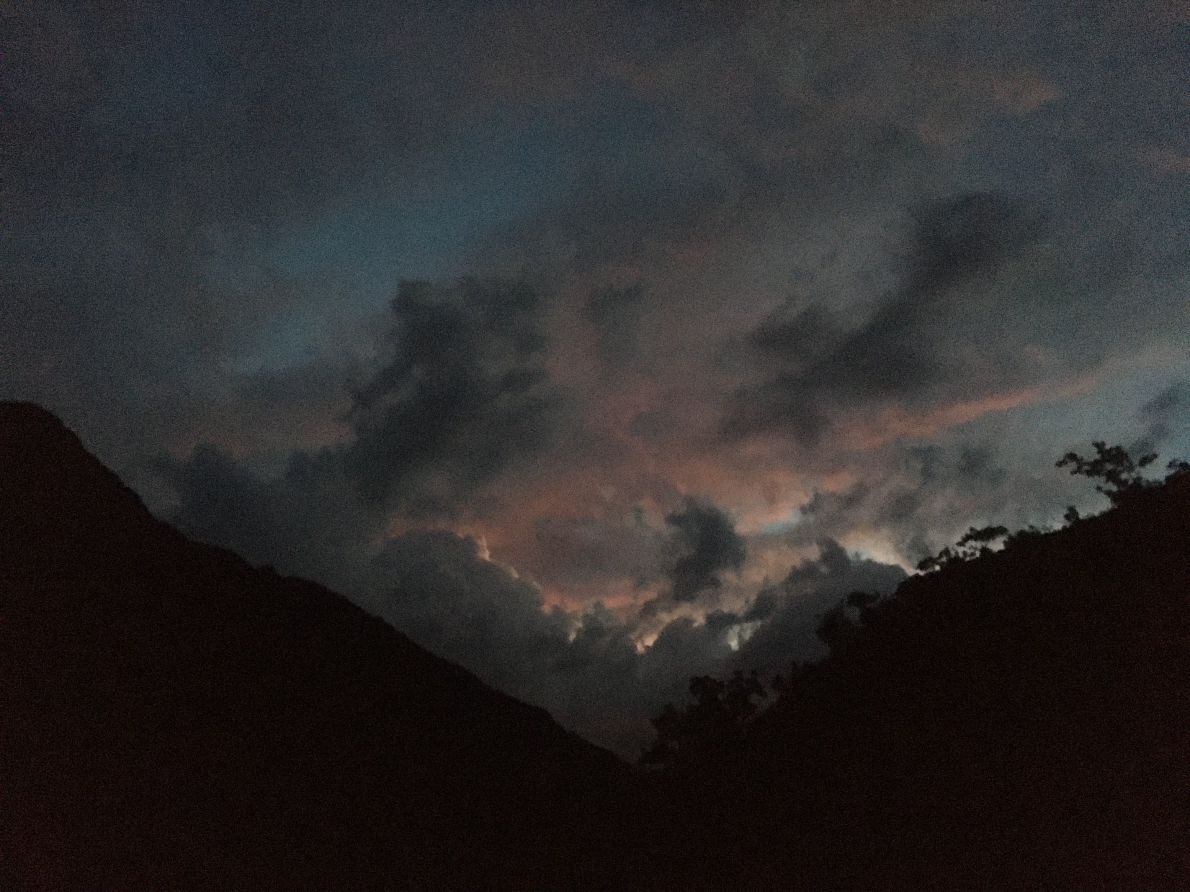 Foto muy oscura. Se intuyen los perfiles de las montañas de un valle y se ven en las nubes los colores rojizos del final del atardecer